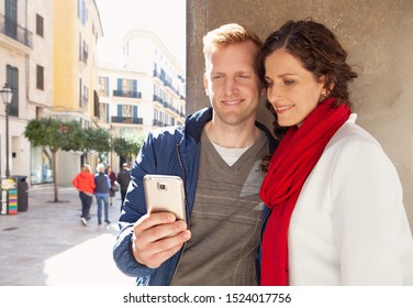 Portrait Beautiful Middle Age Tourist Couple On Sunny Winter City Break Holiday Sightseeing Together, Using Technology Smartphone Smiling, Outdoors. Fun Travel Vacation, Leisure Recreation Lifestyle.