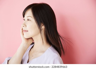 Portrait of a beautiful middle-aged Asian woman, standing in front of a pink wall. Beauty and Health Image. - Powered by Shutterstock