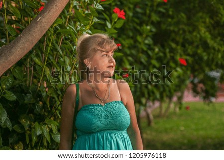 Portrait of a beautiful middle-aged woman with a beautiful figure and big breasts in a beautiful summer dress standing in the park
