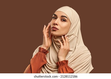 Portrait of beautiful modern muslim woman with natural make-up dressed in beige hijab posing on brown background in studio. Facial skin care, female beauty. - Shutterstock ID 2128112186