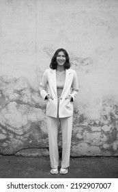 Portrait Of Beautiful Modern Woman In Parking Area. Fashionable. White Suit. Crop Top. Black Hair. Slim And Tall. Daily Life. Work And Leisure. City Background. Black And White Photo