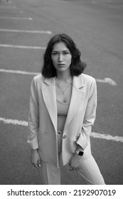 Portrait Of Beautiful Modern Woman In Parking Area. Fashionable. White Suit. Crop Top. Black Hair. Slim And Tall. Daily Life. Work And Leisure. City Background. Black And White Photo