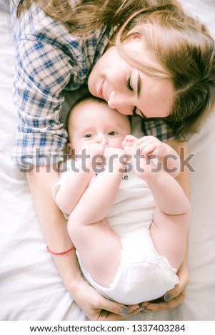 Portrait of beautiful mom in shirt and blue jeans playing with her  baby boy in bedroom - Image

