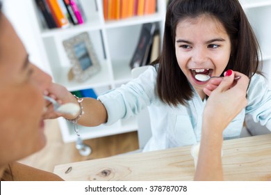 Portrait of beautiful mother and her daughter eating iogurt at home.