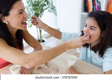 Portrait of beautiful mother and her daughter eating iogurt at home.