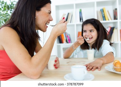 Portrait of beautiful mother and her daughter eating iogurt at home.