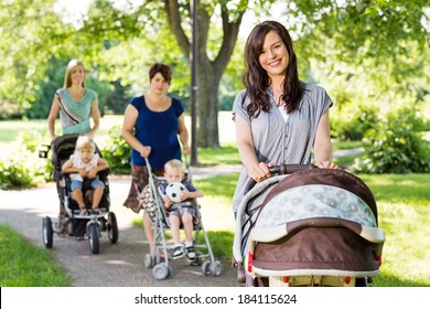 Portrait of beautiful mother pushing baby stroller in park with friends and children in background