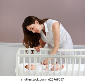 Portrait Of A Beautiful Mother Smiling With Her 3-month-old Baby Near The Crib, Hands, Side View