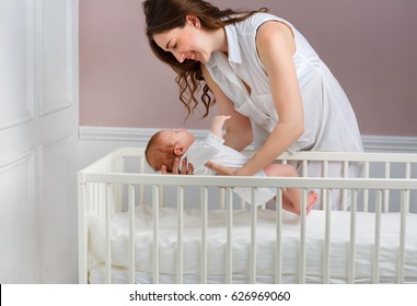 Portrait of a beautiful mother smiling with her 3-month-old baby placed in the baby's crib, side view