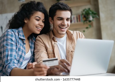 Portrait Of Beautiful Multiracial Couple Shopping Online, Using Laptop Computer.  Happy Friends Ordering Food On Website. Smiling African America Woman Holding Credit Card, Looking At Digital Screen 