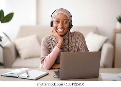 Portrait Of Beautiful Muslim Black Woman In Headscarf Wearing Headset, Communicating Online On Laptop Computer, Indoors. Positive Arab Female Teacher In Hijab Giving Web Lesson From Home