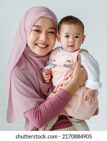 Portrait Of A Beautiful Muslim Woman With A Friendly And Warm Smile Hugging And Cuddling Muslim Infant Baby. Mom Wearing Colorful Hijab Traditional Islamic Dress. Religious And Fimily Concept.