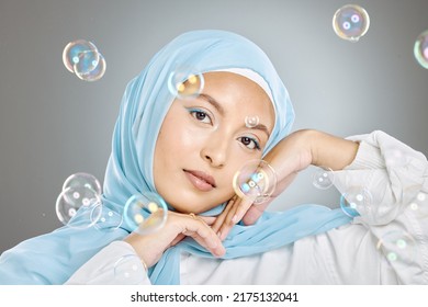 Portrait Of A Beautiful Muslim Woman Wearing Blue Hijab Headscarf Against Grey Background. Arab Female In A Happy Daydream And Fantasy Surrounded By The Pure Delight And Innocence Of Playful Bubbles