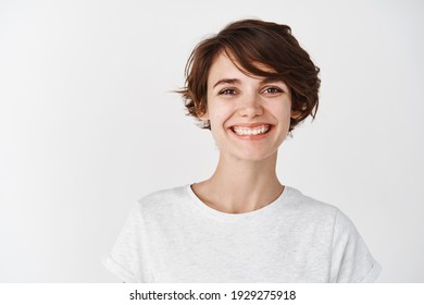 Portrait of beautiful natural girl without makeup, smiling happy at camera, standing in t-shirt against white background.