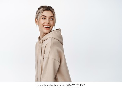 Portrait of beautiful, natural young woman in beige hoodie, turn head, looking behind her shoulder and smiling at logo banner, standing over white background