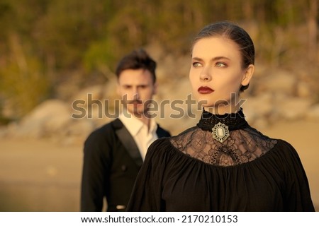 Portrait of a beautiful noble woman rejecting her lover standing behind her on a sea coast. Loving relationship, breakup. Love novel. 19th century style, makeup, fashion.