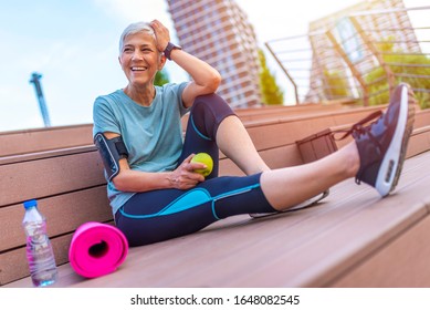 Portrait Of A Beautiful Older Woman With Green Healthy Food After Workout. Portrait Of Fit Mature Woman Smiling While Holding An Apple And Bottle Of Water. Sporty Senior Woman