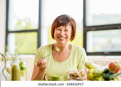 Portrait Of A Beautiful Older Woman With Green Healthy Food On The Table Indoors On The Window Background