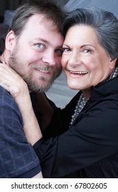 Portrait Of Beautiful Older Woman In Her 70s With Short Black And Grey Hair And Pearl Necklace Hugging Her Grandson