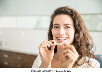 Portrait of beautiful patient holding orthodontic retainers in dental clinic - Shutterstock ID 1121931122