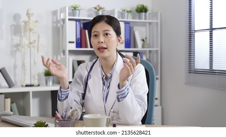 Portrait Beautiful Physician Sitting In Her Office Is Sharing Her Thoughts With Hand Gestures During A Live Medical Webinar At Daytime.