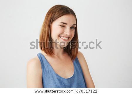Portrait of beautiful playful brunette girl smiling winking looking at camera over white background.
