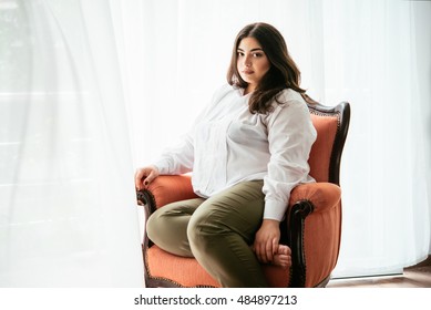 Portrait of beautiful plus size girl in white sitting in the armchair