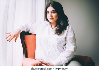 Portrait of beautiful plus size girl in white sitting in the armchair. Toned picture