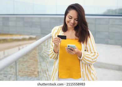 Portrait Of Beautiful Plus Size Woman 30-35 Years Old In Fashion Clothes Made A Payment With A Bank Card Online Through An Application In A Mobile Phone