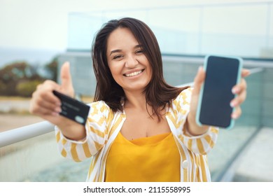 Portrait Of Beautiful Plus Size Woman 30-35 Years Old In Fashion Clothes Doing Online Shopping With Mobile Phone And Bank Credit Card In The City Park Outdoors