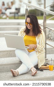 Portrait Of Beautiful Plus Size Woman 30-35 Years Old In Fashion Clothes And Sunglasses Working Remotely On A Laptop On Vacation. Female Freelancer Working On A Computer In The City Park Outdoors