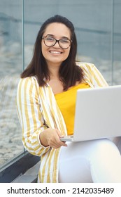 Portrait Of Beautiful Plus Size Woman 30-35 Years Old In Fashion Clothes And Eyeglasses Working Remotely On A Laptop On Vacation. Close-up Female Freelancer Typing On A Computer In The Park Outdoors.