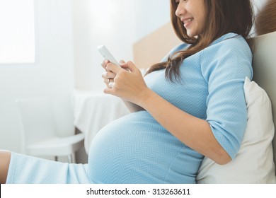 A portrait of a beautiful pregnant woman using mobile phone in her bedroom