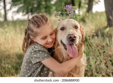 Portrait of beautiful preteen girl petting and hugging golden retriever dog looking at the camera outdoors. Cute female kid with doggy pet at the nature in summer time