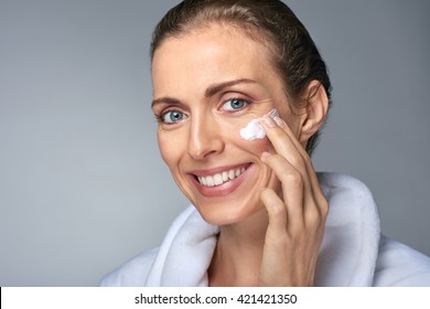 Portrait Of Beautiful Radiant Mature Woman Applying Some Cream To Her Face, Skin Care Cosmetics Wellness Concept