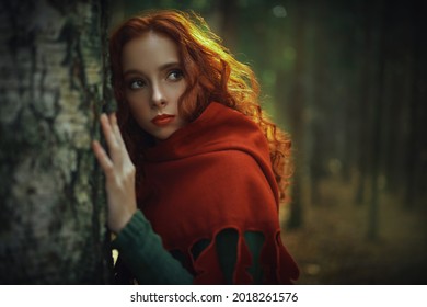 Portrait of beautiful red haired girl in a traditional green celtic dress and a red cloak is in forest. Historical reconstruction of ancient Celtic times.