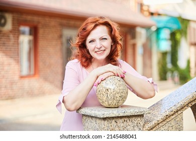 Portrait Of A Beautiful Red-haired Mature Woman In A Pink Dress On The Street.