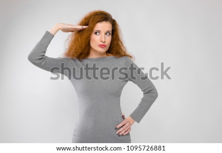 Portrait of beautiful redhead happy smiling young woman in gray clothes showing funny gesture on gray background