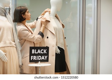 Portrait Of Beautiful Saleswoman Dressing Mannequins In Autumn Clothes While Setting Up Window Display For Black Friday , Copy Space