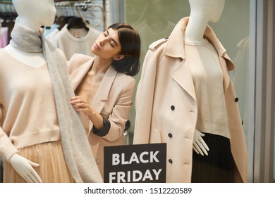 Portrait Of Beautiful Saleswoman Dressing Mannequins In Autumn Clothes While Setting Up Window Display For Black Friday Sale, Copy Space