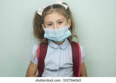 Portrait of a beautiful schoolgirl with a school bag in a medical mask, education concept