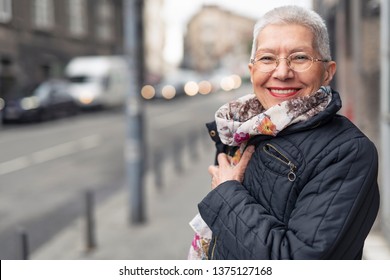 Portrait of beautiful senior woman with a jacket on a windy day in an urban city environment, happy and cheerful