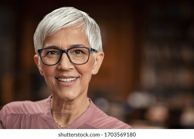 Portrait of beautiful senior woman looking at camera with copy space. Successful mature business woman wearing eyeglasses. Happy old professor in standing in college library with gray hair.