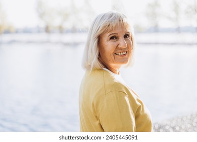 Portrait of beautiful senior woman standing in park spending time on fresh air wearing warm comfy coat. Cute happy senior female looking at camera smiling. - Powered by Shutterstock