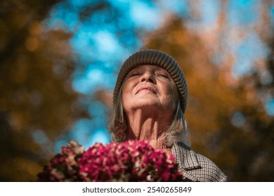 Portrait of a beautiful senior woman standing outdoors with her eyes closed. Autumn nature behind her. - Powered by Shutterstock