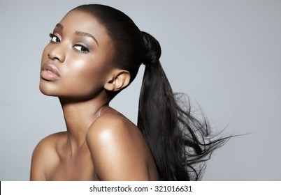 Portrait Of Beautiful Serene African Girl Over Grey Studio Background. African Beauty With Makeup And Long Hair.