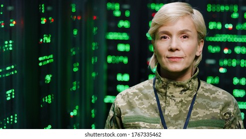 Portrait Of Beautiful Serious Caucasian Military Female Officer In Camouflage Looking At Camera In Dark Monitoring Room. Digital Analytic Center Concept. Close Up Of US Army Woman Among Servers.