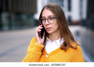 Portrait Of Beautiful Serious Teen Girl, Young Woman Student In Glasses Talking On Cell Mobile Phone, Teenager Calling On Smartphone, Having Conversation Outdoors. 