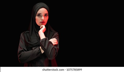 Portrait Of Beautiful Serious Young Muslim Woman Wearing Black Hijab As Conservative Fashion Concept With Hand Near Her Face On Black Background