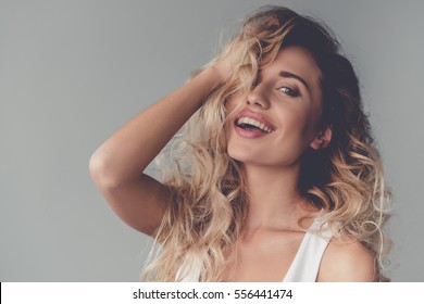 Portrait of beautiful sexy blonde girl touching her hair and smiling, on gray background